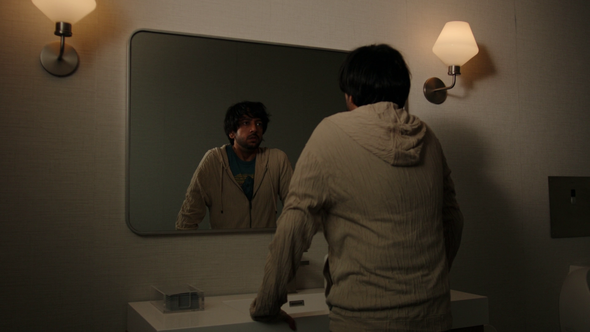 Vik leans over a bathroom sink and looks into the mirror in Cupertino episode 2.
