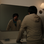 Vik leans over a bathroom sink and looks into the mirror in Cupertino episode 2.