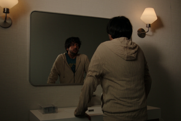 Vik leans over a bathroom sink and looks into the mirror in Cupertino episode 2.