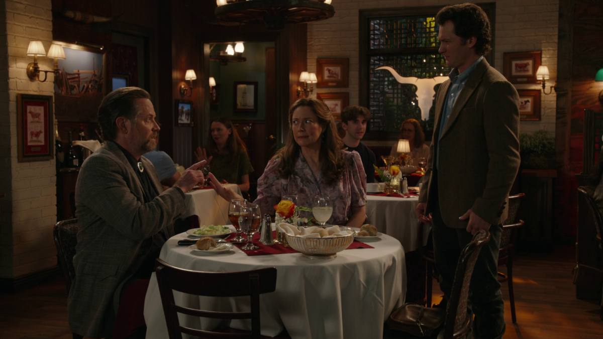 Mary and Fagenbacher at their restaurant table while Georgie stands beside them, looking down at the date he’s about to interrupt.
