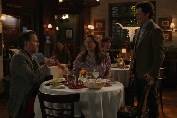 Mary and Fagenbacher at their restaurant table while Georgie stands beside them, looking down at the date he’s about to interrupt.