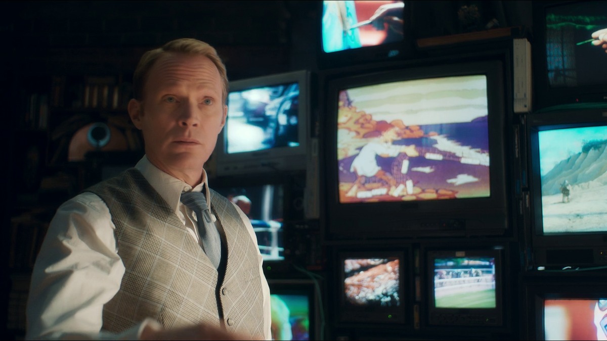 VisionQuest Ship of Theseus: Vision in a waistcoat and tie in front of a wall of old TVs in his mindscape